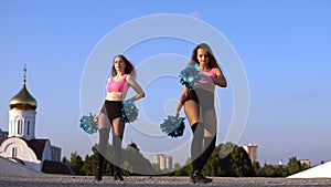 Two girls cheerleaders with pompons dancing outdoors