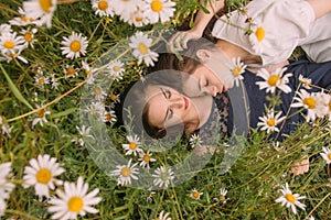 Two girls with closed eyes in dark blue and white dresses in sunny day lying down  and sleeping in chamomile field