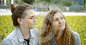 Two girls closeup portrait sitting among fields of sunflowers and talking while discussing something. One girl is curly