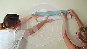 Two girls at construction site glues wallpaper to the wall