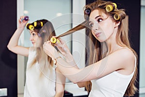 Two girls curling their hair with rollers in a room