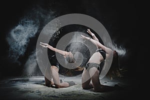 Two girls dance with flour in studio on black background, lights behind them and people helped girls