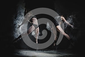 Two girls dance with flour in studio on black background, lights behind them and people helped girls