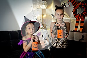 Two girls disguised as a tiger and as a witch are waiting for some candies in All Saints' Day.