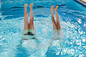 Two girls are doing handstand in a swimming pool in the summer