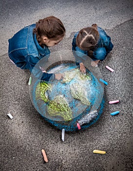 Two girls drawing realistic Earth image with chalks on ground