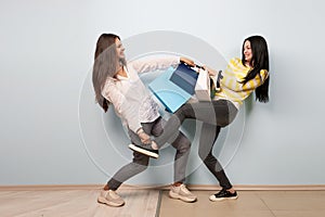 Two girls dressed in nice casual clothes fight and take each other shopping bags on the white background