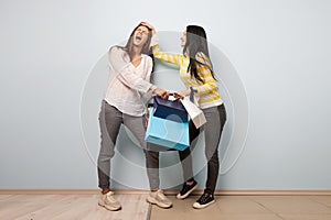 Two girls dressed in nice casual clothes fight and take each other shopping bags on the white background