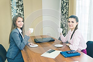 Two girls drink coffee at the workplace during a break.