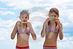 Two girls eat watermelon on the beach against the cloudy sky