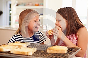 Two Girls Eating Cheese On Toast In Kitchen