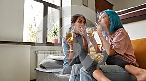 Two girls eating popcorn and drinking wine on sofa