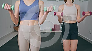 Two girls exercising dumbbells at home closeup. Athletic women training arms