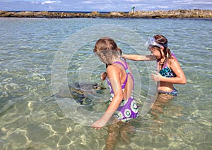 Two girls feed a sea turtle