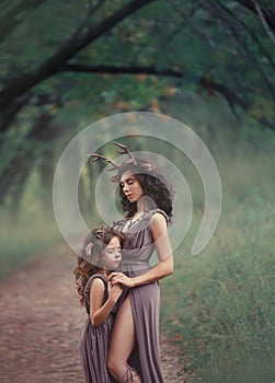 Two girls in the form of deer hug and close their eyes, fauns in long brown dresses, a cutout reveals the mothers bare