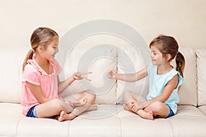 Two girls friends playing rock paper scissors hand game. Caucasian children sitting on a couch playing together. Interesting