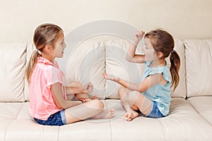 Two girls friends playing rock paper scissors hand game. Caucasian children sitting on a couch playing together. Interesting