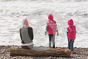 Two girls and a girl on beach sitting on a log and looking into the distance