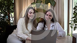 Two girls girlfriends communicate and drink coffee using a laptop making a video call while sitting in a cafe spending
