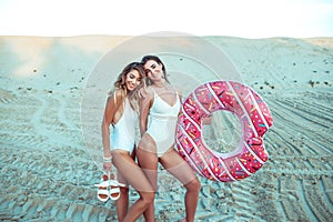 Two girls girlfriends standing sand with inflatable circle, beautiful women beach white bodysuit. Holidays sea on ocean