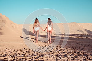 Two girls girlfriends walking sand view from rear, beautiful women sunbathes summer beach white bodysuit. Rest sea on
