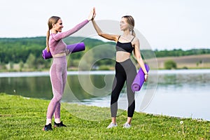 Two girls give each other high five after a good training session in the park near lake. Attractive sporty women smiling outdoor