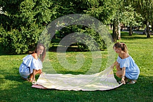 Two girls on a green meadow spread out a picnic blanket. Summer weekends photo