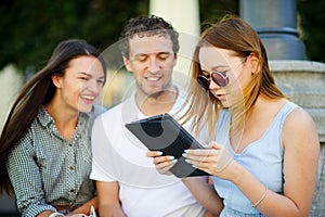 Two girls and the guy with interest look at the tablet screen.