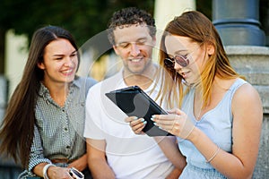 Two girls and the guy with interest look at the tablet screen.