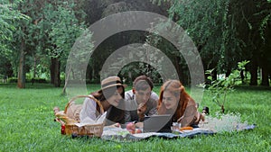 Two girls and a guy are lying on a picnic in the summer in nature and watching a movie on a tablet