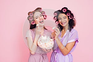 Two girls with hair curlers eating marshmellows. They are celebrating women`s day March 8.