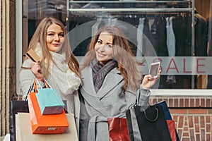 Two girls are happy with a credit card in front of show-window with sale written on it