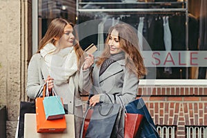 Two girls are happy with a credit card in front of showwindow wi