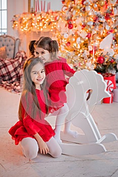 Two girls have fun riding toy horse in front of a Christmas tree