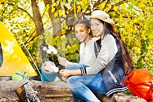 Two girls hold marshmallow sticks near bonfire