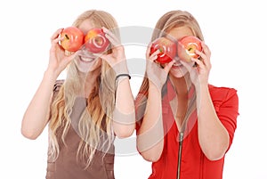 Two girls hold near eyes fresh apples