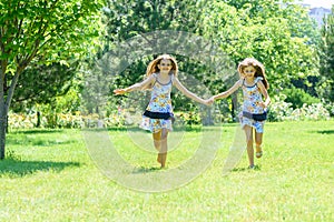 Two girls holding hands run on a green lawn in a park