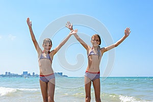 Two girls joyfully raised their hands up on the seashore