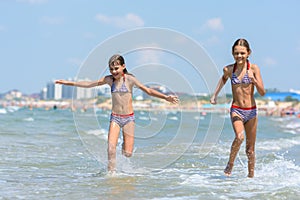 Two girls joyfully run along the seashore on a warm summer day