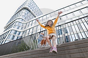 Two girls jumping down from concrete wall in city. Low angle view.