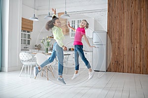 Two girls jumping in the kitchen feeling happy