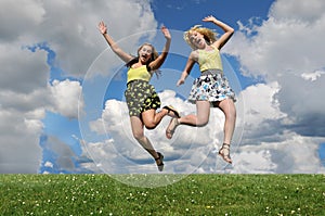 Two girls jumping over grass hill