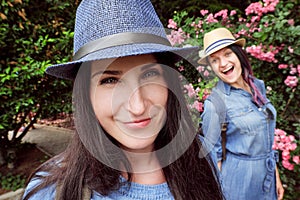 Two girls laugh, posing in the garden with blooming roses on a fisheye lens