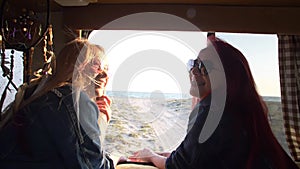 Two girls are laughing against the background of the autotrailer behind which the seashore