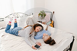 Two girls laughing and holding mobile phones while lying in bed together