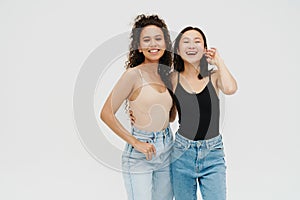 Two girls laughing while posing isolated over white studio wall