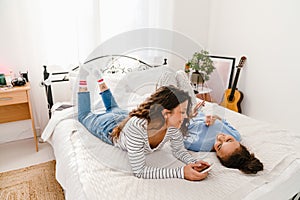 Two girls laughing and using mobile phones while lying in bed together