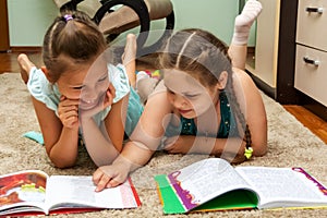 Two girls lie on the carpet and cheerfully look at the books