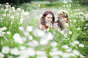 Two girls lie on a green meadow with white daisies