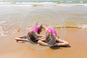 Two girls lie on your back on sandy beach and looking at sea